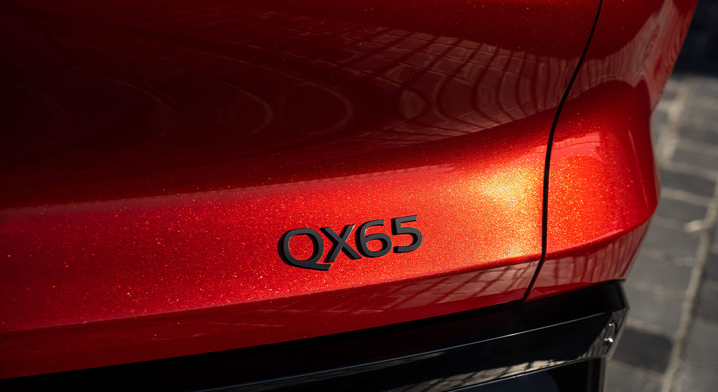 Close-up of the rear of a shiny red Infiniti car displaying "QX65" in black text representing car model number  . The metallic paint glimmers in sunlight, evoking a sleek, modern aesthetic.